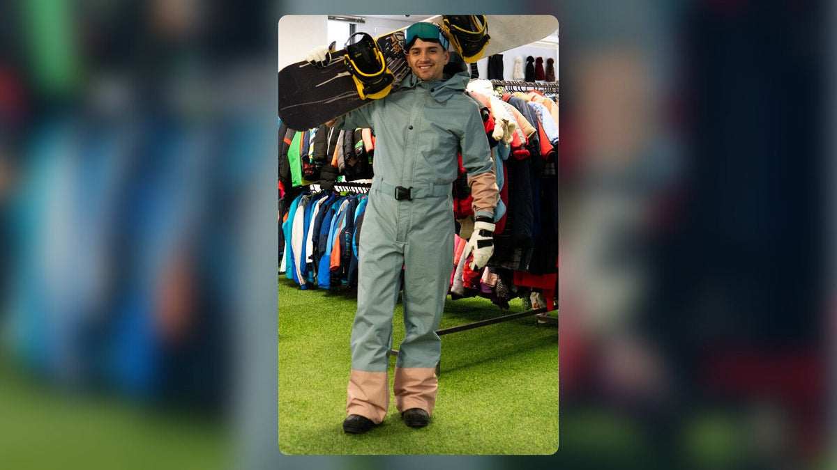 Joven con tabla de snowboard arrendada y enterito de nieve en la tienda Andes Premier Rental en Las Condes